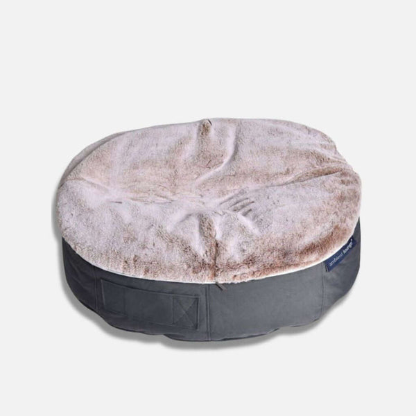 En rund, plyschig hundeseng från Ambient Lounge med en mjuk, ljusbeige fuskpäls på ovansidan och en mörkgrå bas - denna eleganta hundeseng cappuccino visas på en vanlig ljus bakgrund.