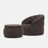 En modern, mörkbrun fåtölj i quiltat tyg med en matchande ottoman i memory foam, båda med mjuka, rundade former och subtila sömnadsdetaljer, mot en vit bakgrund.