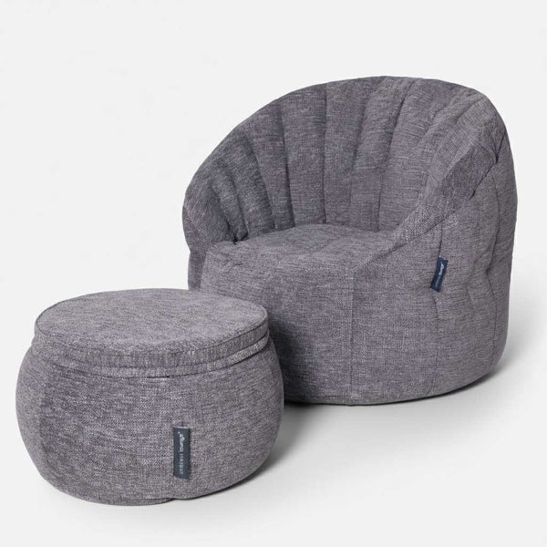 En modern, grå stoppad stol med rundad rygg och vertikala sömdetaljer, tillsammans med en matchande rund ottoman, framkallar elegansen hos en Butterfly Chaise, båda mot en vit bakgrund.