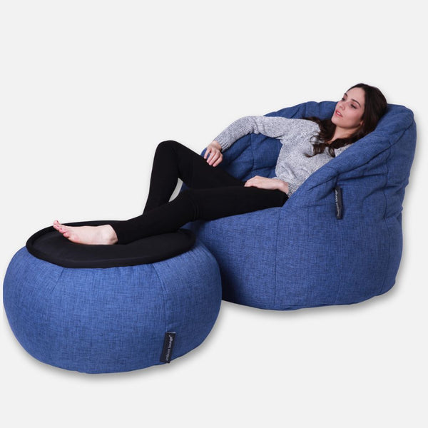 En kvinna slappnar av bekvämt på en Ambient Lounge Cove Package, med fötterna vilande på en matchande blå ottoman-designer sittegruppe mot en vit bakgrund.