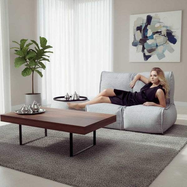 En kvinna i svart klänning slappnar av i en flexibel soffa i ett modernt vardagsrum med soffbord i trä, krukväxt, abstrakt väggkonst och mjukt naturligt ljus från höga fönster.