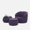 Contempo Indoor Package har en modern design med tre lila, bekväma möbler: en stoppad stol, en rund ottoman och ett litet bord med en bärbar dator, allt mot en vit bakgrund.