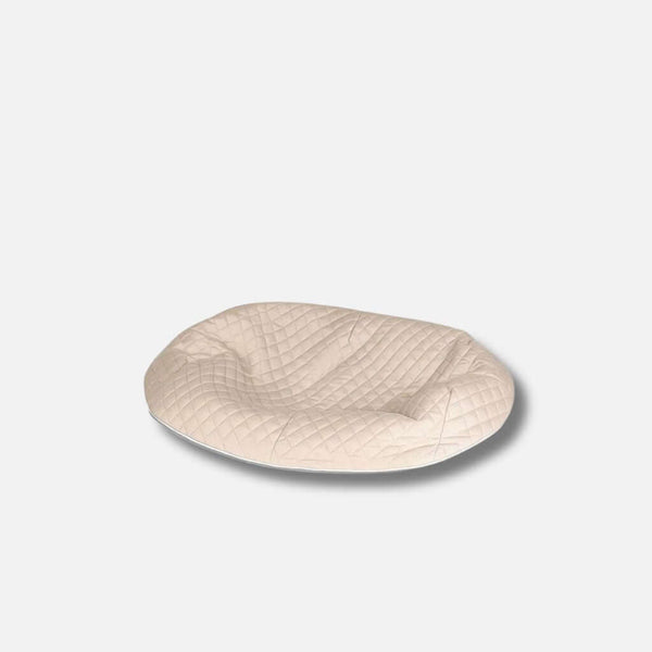 En beige, ovalformad allergivennlig hundeseng med quiltat toppdrag, med en lätt indragen yta, mot en enfärgad vit bakgrund.