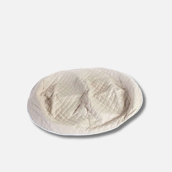 En stor, rund, beige ThermoQuilt hundeseng med quiltat toppdrag och en lätt indragen mitt, perfekt som allergivennlig hundeseng. Placerad på en enfärgad vit bakgrund.