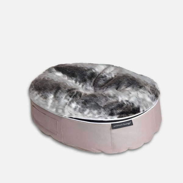 En rund, plyschig hundesäng med en mjuk topp i fuskpäls i grå, vita och svarta nyanser och en bas i ljusbeige tyg. Sängen har en etikett på sidan och är placerad mot en enfärgad vit bakgrund.
