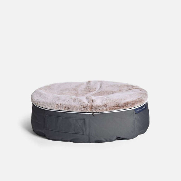En rund, grå hundeseng från Ambient Lounge med mjuk, ljusbrun fuskpäls på ovansidan, vilket ger optimal komfort för hund, står på en vit bakgrund.
