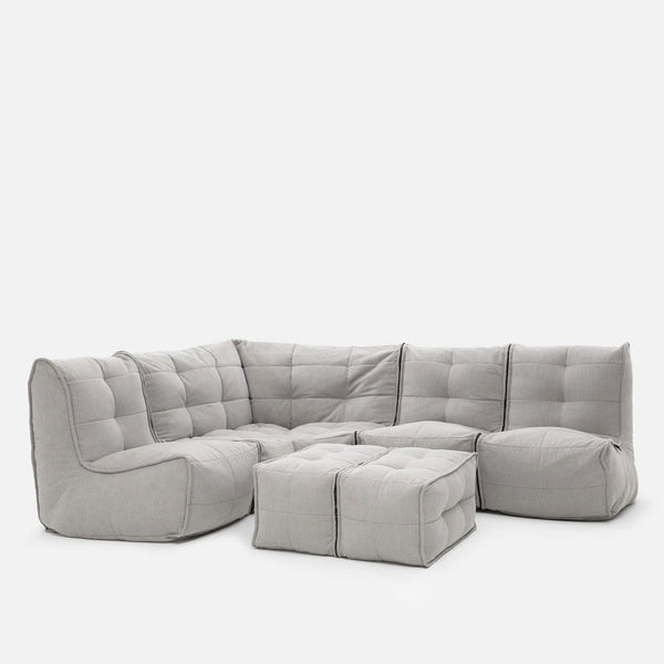En modern, modulär ljusgrå Modulsoffa med två matchande ottomaner, med mjuk, tuftad klädsel och plyschiga, lådformade kuddar - perfekt för hjemmekino-møbler - arrangerade i L-form mot en vit bakgrund.
