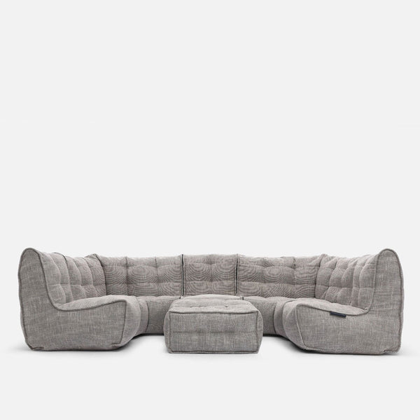 En stor, modern Ambient Lounge modulær-soffa med ljusgrå tuftade kuddar och en ottoman i mitten skapar en elegant, modern stueløsning mot en vit bakgrund.