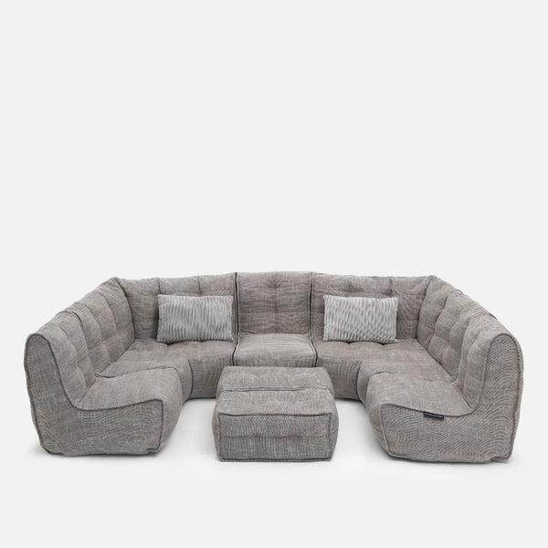 En modern, grå modulær-soffa med tuftad klädsel placerad i en U-form, med tre matchande rektangulära kuddar och en fyrkantig ottoman i mitten - allt skapar en elegant, modern stueløsning mot en vanlig vit bakgrund.