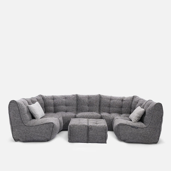 En modern grå modulær soffa med tuftade kuddar, två matchande ottomaner och två accentkuddar, placerade i en U-form mot en vit bakgrund - en perfekt modern stueløsning från Ambient Lounge.