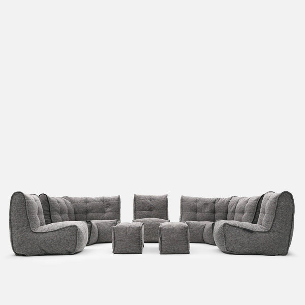 A modulær sofa fra Ambient Lounge, denne moderne stueløsning har tuftet puter og består av to hjørnedeler, to armløse deler og fire puffer, arrangert i en U-form på hvit bakgrunn.
