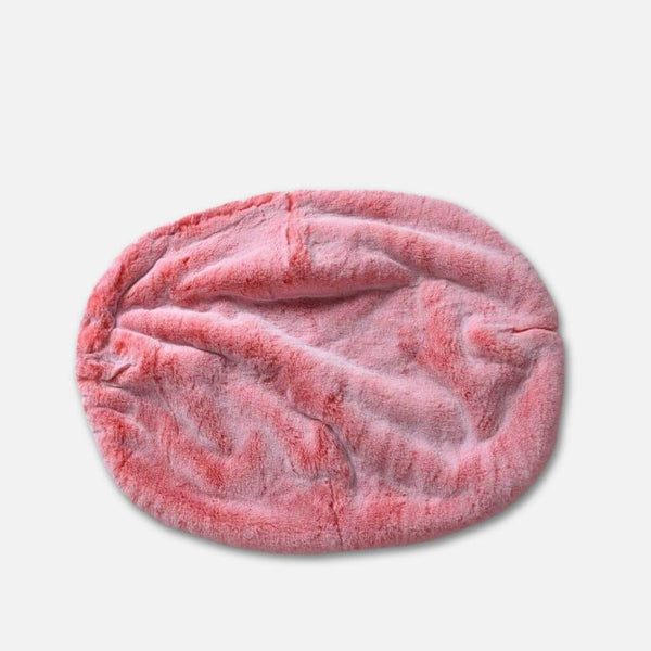 En mjuk, ovalformad rosa plyschhundeseng med en luksuriøs pelstopp visas på en vit bakgrund.