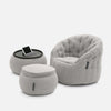 En modern, ljusgrå, quiltad fåtölj från Contempo Indoor Package sitter tillsammans med en matchande ottoman och ett runt sidobord med en surfplatta, allt mot en vit bakgrund.