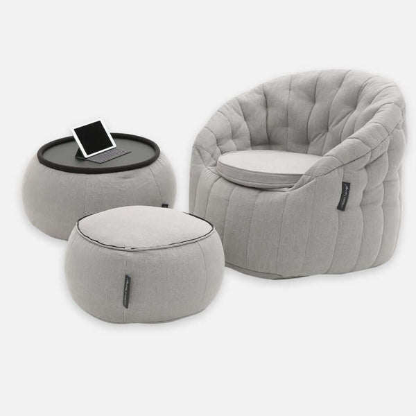 En modern fåtölj i ljusgrått tyg från Contempo Indoor Package med en matchande ottoman och ett litet runt sidobord med en surfplatta, allt mot en vit bakgrund.