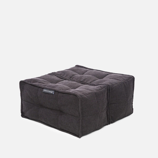 En fyrkantig, mörkgrå, tuftad Twin Ottoman golvdyna från Ambient Lounge, med en tygetikett på framsidan, ligger mot en vit bakgrund - perfekt för fans av moderna möbler.