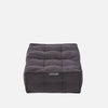 En fyrkantig, mörkgrå, tuftad Twin Ottoman från Ambient Lounge med en mjuk tygstruktur och en liten etikett på framsidan, som visar modern möbelstil mot en vit bakgrund.
