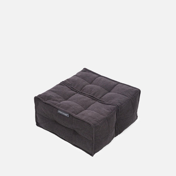 En mörkgrå, kvadratisk golvdyna från Ambient Lounge med en kviltad, tuftad design, lätt upphöjda kanter och en tygetikett på framsidan - en idealisk Twin Ottoman för att ge modern møbler-stil till alla utrymmen.